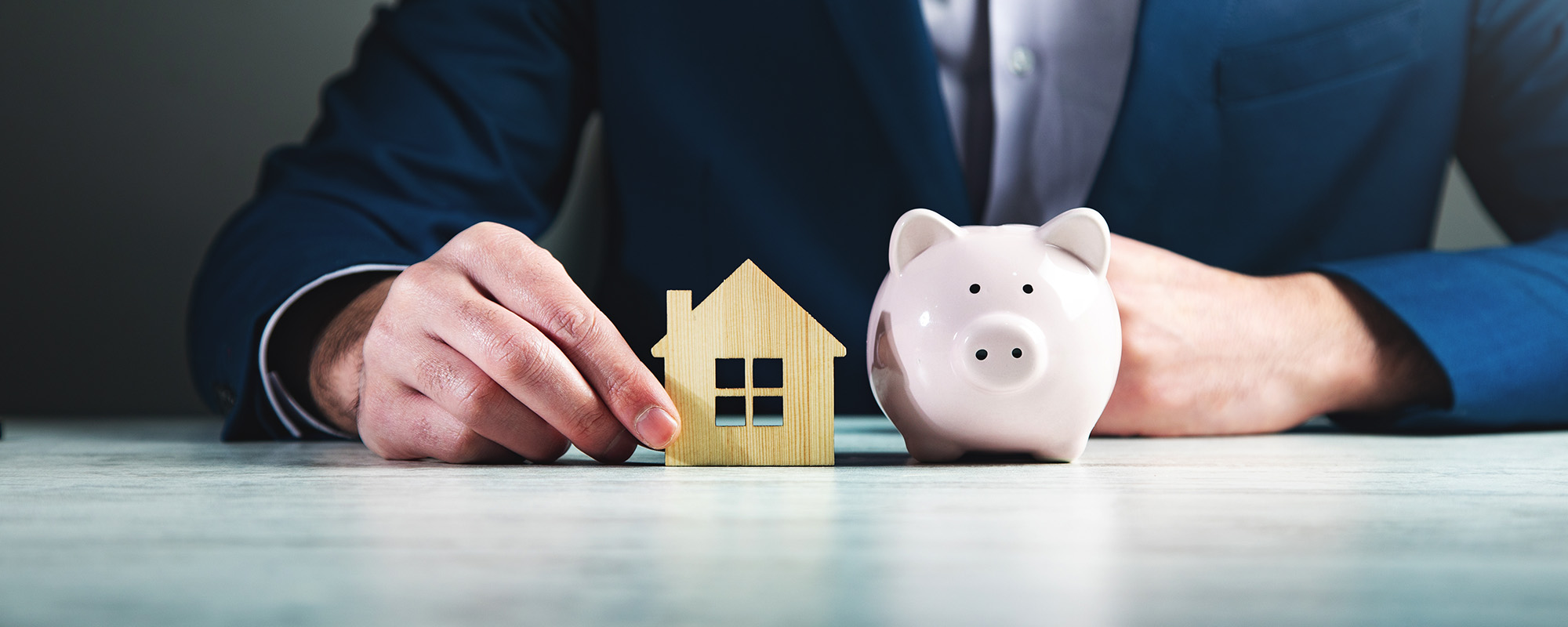 businessman holding wooden house and piggy bank 