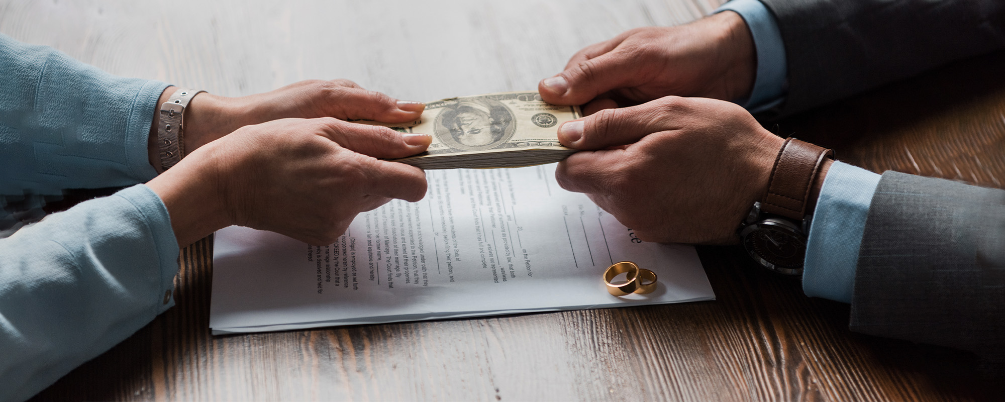 partial view of lawyer and client holding dollar banknotes above divorce decree with wedding rings 