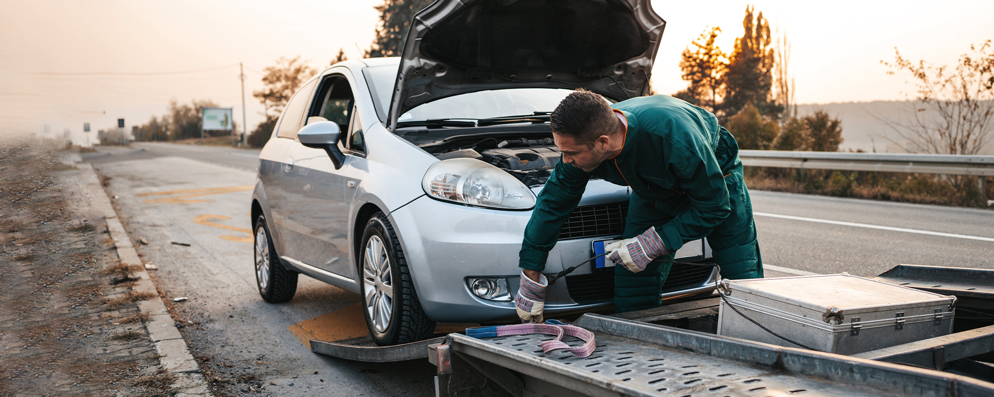 road assistant worker in towing service trying to start car engine with jump starter and energy station with air compres