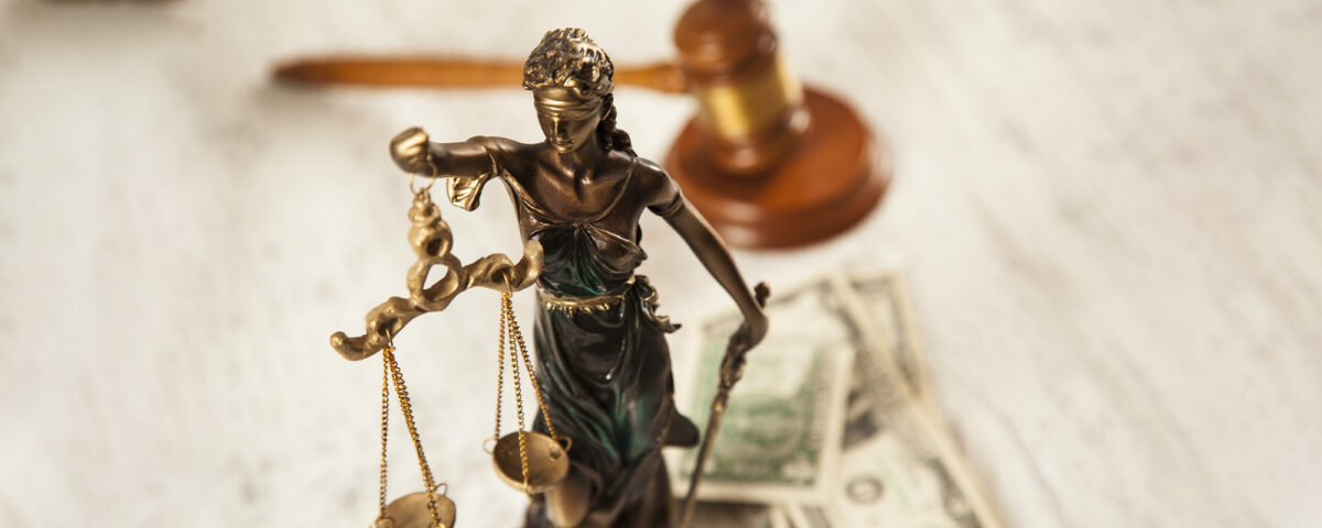 Lady Justice statue and money on s wooden desk with judge's gavel;